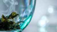 Dried herbs steaming in glass cup with hot water, herbal tea preparation for wellness and natural remedies.