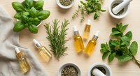 Fresh herbs and essential oils arranged on wooden surface with mortar and pestle for natural aromatherapy and cooking preparations.