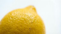 Fresh yellow lemon with water droplets on textured peel surface isolated on white background for culinary and beverage design projects.
