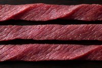 Fresh raw beef slices showing natural meat texture and marbling pattern on dark wooden background, close-up view for culinary and food industry use.