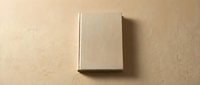 Closed hardcover book with blank beige linen cover on neutral tan background, ready for branding, publishing, or design mockup projects.