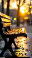 Empty park bench covered in autumn leaves at sunset, with golden bokeh lights and sun flare creating magical atmosphere. Silhouette against warm evening light.