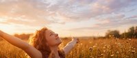 Young woman with curly hair celebrating freedom in golden wheat field at sunset with arms raised expressing joy and happiness in nature.