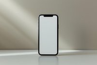 Modern smartphone with blank white screen standing upright on light surface against neutral background, mockup ready for app or website presentation.