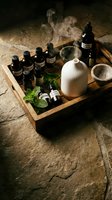 Natural aromatherapy essential oils collection in wooden tray with ceramic diffuser and mortar pestle on rustic stone surface for wellness spa treatments.