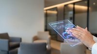 Young woman with light skin tone wearing white long-sleeve shirt holding transparent futuristic touchscreen tablet displaying holographic data interface in modern office lobby setting.