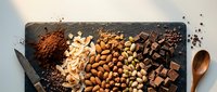 Assorted nuts, chocolate pieces, cocoa powder and spices arranged on dark slate board. Premium ingredients for baking, cooking and confectionery preparation.