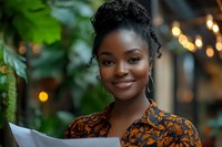 Young African American businesswoman smiling while holding documents in modern office with plants and warm lighting for professional corporate content.