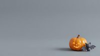 Carved jack-o-lantern pumpkin with glowing face next to small gray bat figurines on neutral background, suitable for Halloween seasonal designs and decorations.