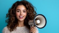Young mixed-race woman with curly hair and bright smile holding megaphone against turquoise background, expressing joy and confidence while making announcement.