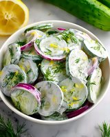 Fresh cucumber salad with creamy yogurt dressing, sliced red onions and dill garnish in white bowl, served with lemon. Healthy Mediterranean side dish.