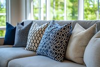 Modern living room interior with decorative throw pillows on gray sofa near bright windows showcasing contemporary home decor and comfortable seating area.