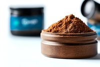 Brown protein powder supplement in wooden container with blurred supplement jar in background, macro photography showing texture and detail.