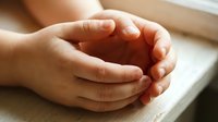 Hands clasped together in prayer or meditation position on wooden surface, expressing faith, spirituality, hope and peaceful contemplation in warm natural light.