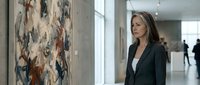 Professional businesswoman in dark suit contemplating abstract artwork in modern gallery space with natural lighting and contemporary interior design.