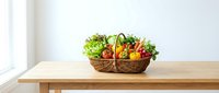 Wicker basket filled with fresh vegetables including lettuce, tomatoes, peppers and cucumbers on wooden table by window for healthy eating and organic produce concepts.