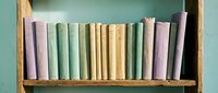 Vintage books with pastel colored spines arranged on wooden shelf creating cozy library atmosphere for home decor and reading concepts.