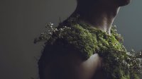 Young woman with moss covering shoulders and chest in artistic nature-inspired portrait showcasing organic textures and environmental harmony concept.