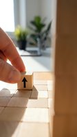 Hand placing wooden block with upward arrow on stacked cubes representing business growth, success and strategic planning in modern office environment.