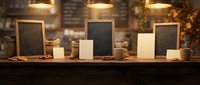 Cozy coffee shop counter with blank chalkboard signs, white paper bags and warm pendant lighting creating inviting cafe atmosphere for menu displays.