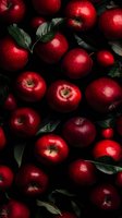 Fresh red apples with green leaves scattered on dark background, dramatic moody lighting highlights glossy fruit surface, creating contrast between bright apples and shadows.