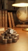 Stacks of vintage coins on wooden desk with antique lamp, globe and books creating warm scholarly atmosphere for financial education concepts.