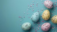Speckled pastel Easter eggs in blue, yellow, pink and mint colors scattered with tiny heart confetti on turquoise background. Modern holiday composition.