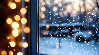 Snowy winter evening view through window with warm glowing bokeh lights and falling snowflakes creating cozy festive atmosphere for seasonal designs.