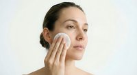 Young woman applying skincare product with cotton pad on face during daily beauty routine for healthy glowing skin and facial care regimen.