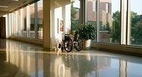 Empty wheelchair in bright hospital corridor with large windows and polished floors creating peaceful healthcare environment for patient mobility assistance.
