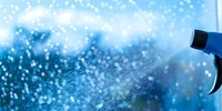 Water spray from blue bottle creating misty droplets against blurred blue background, suitable for cleaning and freshness concepts.