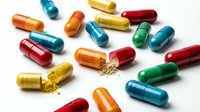 Colorful pharmaceutical capsules scattered on white background with some opened showing powder content for medical and healthcare concepts.