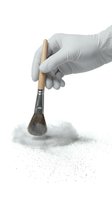 Gloved hand holding wooden brush with natural bristles applying fine powder or dust on white background for restoration, cleaning, or artistic work.