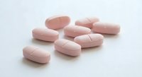 Pink oval pharmaceutical tablets scattered on white background for medical and healthcare concepts.