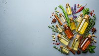 Various essential oils in glass bottles with fresh herbs, spices and aromatherapy ingredients arranged on textured background for natural wellness and spa treatments.