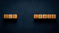 Buy or lease decision concept with wooden blocks on dark textured background for real estate, property investment, and financial planning materials.
