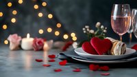 Romantic dinner setting with heart decorations, rose gold wine, macarons, roses and candles on dark table against blurred bokeh lights background.