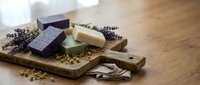 Natural handmade soap bars with dried lavender flowers on rustic wooden cutting board for organic skincare and aromatherapy spa treatments at home.