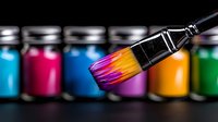 Paint brush with vibrant rainbow colors against blurred background of colorful paint jars, showing artistic creativity and professional painting supplies.