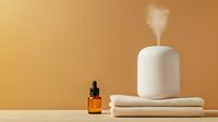 White essential oil diffuser releasing aromatic mist on folded towels with amber dropper bottle against warm beige background for spa wellness relaxation.