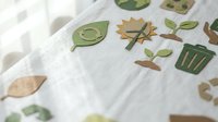 Eco-friendly paper cutout icons featuring trees, leaves, recycling symbols and green elements scattered on white fabric background for sustainable design projects.
