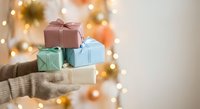 Hands in cozy sweater holding colorful wrapped gift boxes with warm bokeh lights creating festive holiday atmosphere for celebrations and giving.