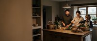 Happy family cooking together in modern kitchen with father and children preparing healthy meal at wooden counter during evening time.