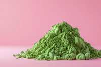 Green matcha powder pile on pink background for healthy lifestyle and wellness concepts.