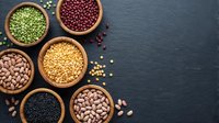 Assorted legumes and pulses in wooden bowls on dark slate background. Variety of beans, lentils and peas for healthy cooking and plant-based nutrition.