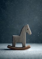 Wooden rocking horse toy on dark background with falling snow effect, creating nostalgic holiday atmosphere for childhood themes.