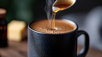Steaming hot chocolate in black mug with honey or maple syrup drizzle creating artistic pour, close-up on dark background with bokeh effect. Food photography.