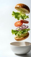 Floating burger ingredients with sesame bun, lettuce, tomato and onion falling into white bowl on clean background for food advertising and menu design.
