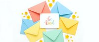 Colorful pastel envelopes arranged around a be kind greeting card with yellow flowers on white background, flat lay top view.