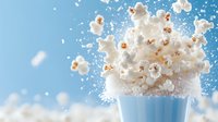 Fresh popcorn explosion from light blue striped container against blue background with flying kernels and dramatic motion capture for food advertising.
